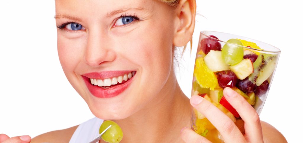 Closeup of beautiful young woman holding glass full of mixed fruits
